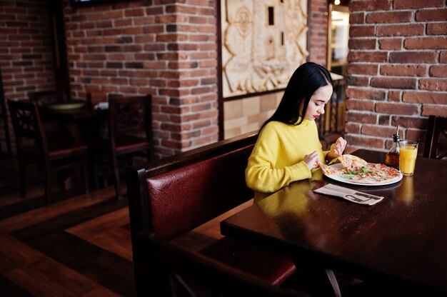 Śmieszna brunetki dziewczyna w żółtej puloweru łasowania pizzy przy restauracją.