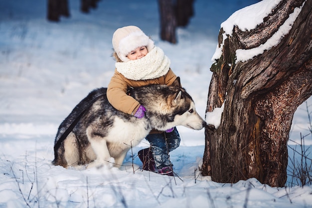 Śmieszna Mała Dziewczynka Przytulanie Swojego Dużego Psa Malamute Zimą W Lesie