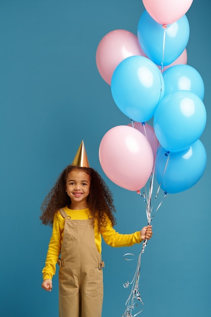 Śmieszna Mała Dziewczynka W Czapce Trzyma Kilka Kolorowych Balonów. ładne Dziecko Dostało Niespodziankę, Imprezę Lub Przyjęcie Urodzinowe