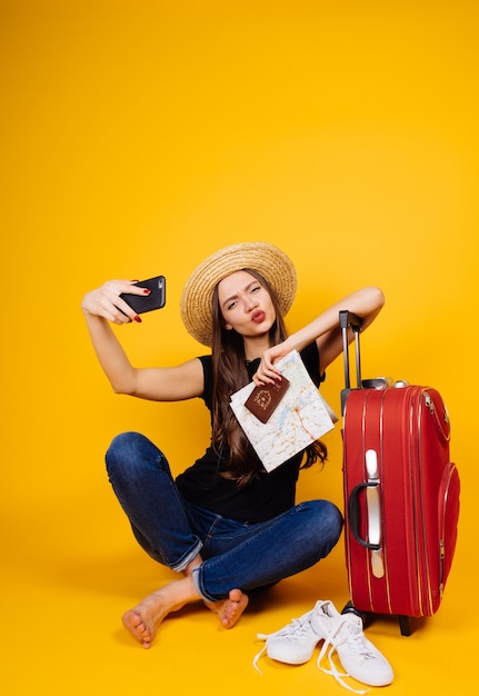 Śmieszna Młoda Dziewczyna W Kapeluszu Podróżuje Na Wakacje, Z Dużą Czerwoną Walizką, Robi Selfie