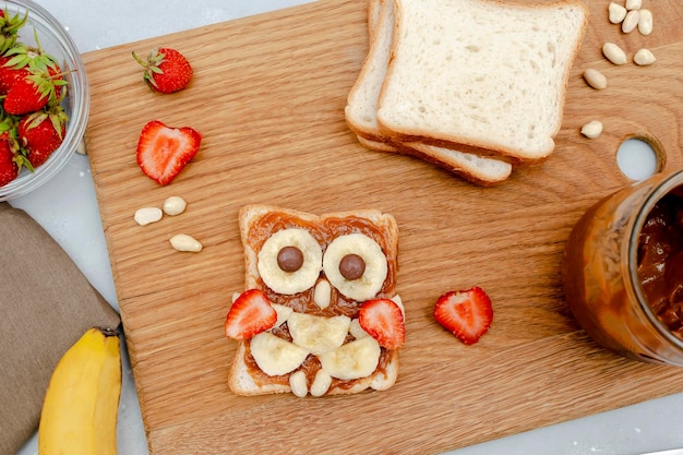 Śmieszna sowa buzia kanapka chleb tostowy z masłem orzechowym banan truskawka na desce słodkie dzieci dla dzieci słodki deser dla dzieci zdrowe śniadanieobiad sztuka jedzenie na szarym tlewidok z góry