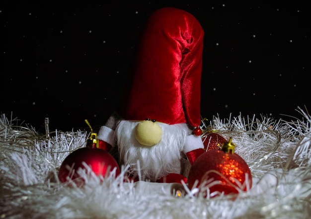 Śmieszna zabawka Świąteczny gnom w czerwonym kapeluszu otoczonym czerwonymi dekoracjami świątecznymi