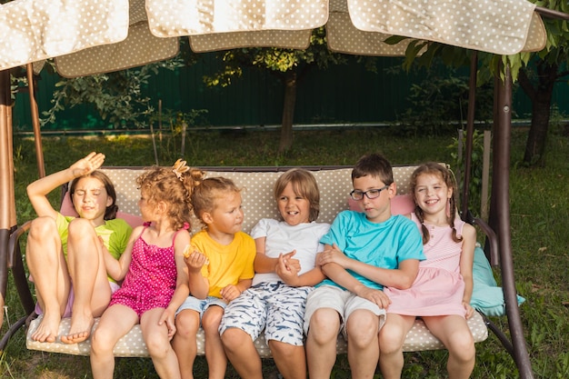 Śmieszne dzieci odpoczywające na dużej huśtawce ogrodowej