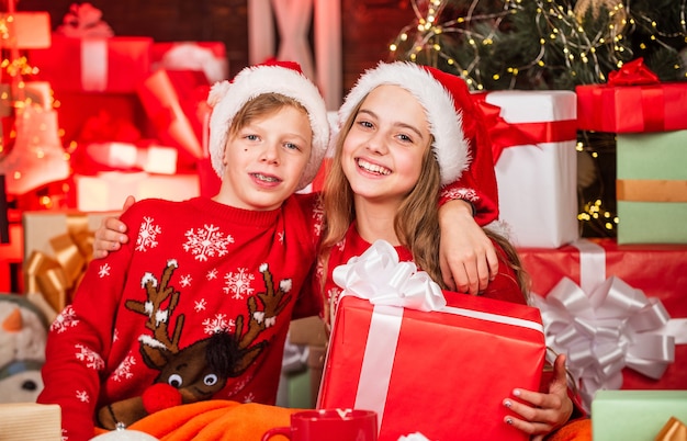 Śmieszne dzieciaki. Sklep z pamiątkami. Dzieciak santa hat świąteczne pudełka na prezenty. Wesołych Świąt. Piękno zimy. Wypoczynek i aktywność. Rodzinna zabawa. Dzieci mała szczęśliwa dziewczynka i chłopiec znajdują prezenty w pobliżu choinki.