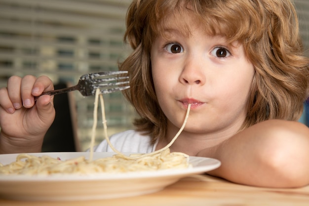 Śmieszne dziecko jedzenie makaronu, spaghetti, twarz z bliska. Portret głowy dzieci.