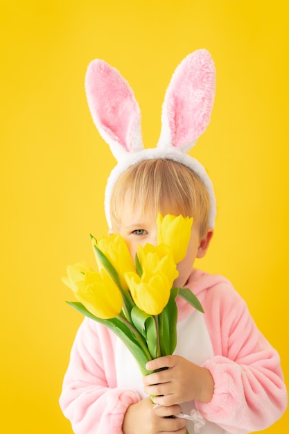 Śmieszne Dziecko Nosi Uszy Królika Wielkanocnego I Trzyma Bukiet Tulipanów Na żółtej ścianie.