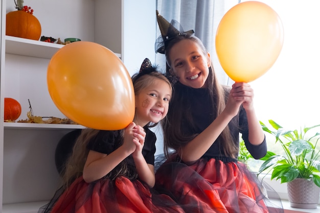 Śmieszne dziewczyny w halloweenowych kostiumach wiedźmy z balonami świętują święto z radością