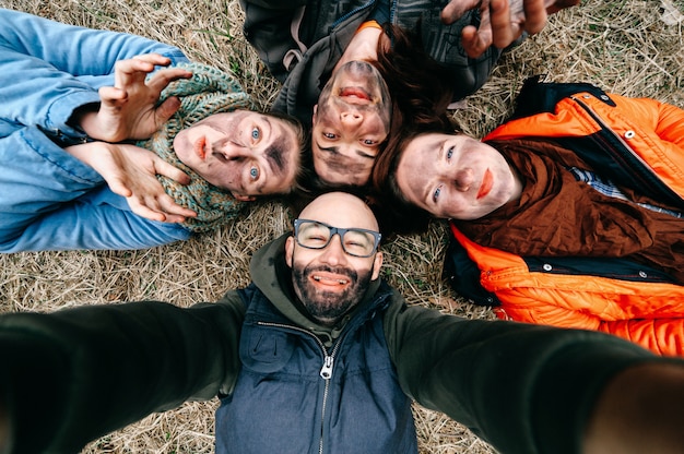 Zdjęcie Śmieszne selfie. grupa przyjaciół z brudnymi poplamionymi twarzami wygłupia się. komiks przerażające szalone upiorne wyraziste twarze. grupa czterech osób leżących na trawie. dwóch mężczyzn z parą kobiet korzystających z imprezy.