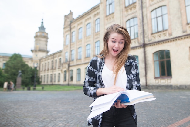 Śmieszny student student student stoi na kampusie na uniwersytecie i ze zdumieniem patrzy na książkę w swoich rękach