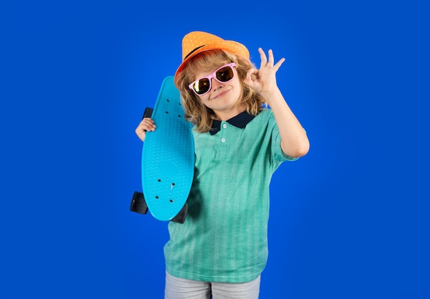 Śmieszny szczęśliwy dzieciak w przypadkowej odzieży trzyma longboard patrzeje szczęśliwego i z podnieceniem Pracowniany odosobniony portret