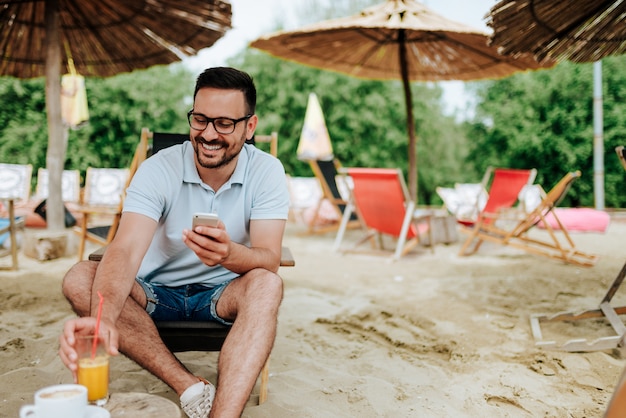 Smilling Mężczyzna Pije Koktajl Przy Plażą I Używa Telefon.