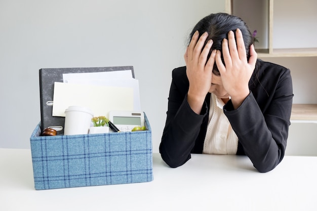 smutek całkiem żeński pracownik biurowy jest zwolniony pakowanie rzeczy osobistych siedzi na biurko pracy uczucie zdenerwowany i myślenia przyszłej pracy.