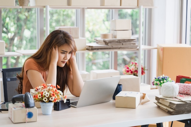 Smutna azjatycka młoda kobieta biznesu trzymać głowę ręką z uczuciem zmartwienia lub depresji, ponieważ problem biznesowy przez laptop w jej domowym biurze uruchamiania, stres kobiety z koncepcji pracy