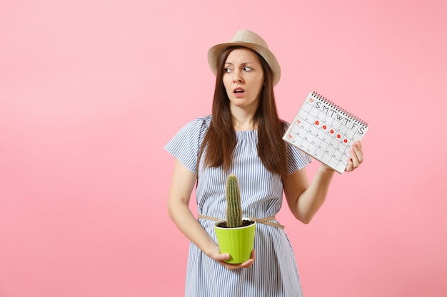 Smutna Choroba Kobieta W Niebieskiej Sukience, Trzymając Zielony Kaktus, Kalendarz Okresów Do Sprawdzania Dni Menstruacji Na Białym Tle Na Różowym Tle. Medycyna, Opieka Zdrowotna, Ginekologiczna, Koncepcja Bólu Brzucha. Skopiuj Miejsce.