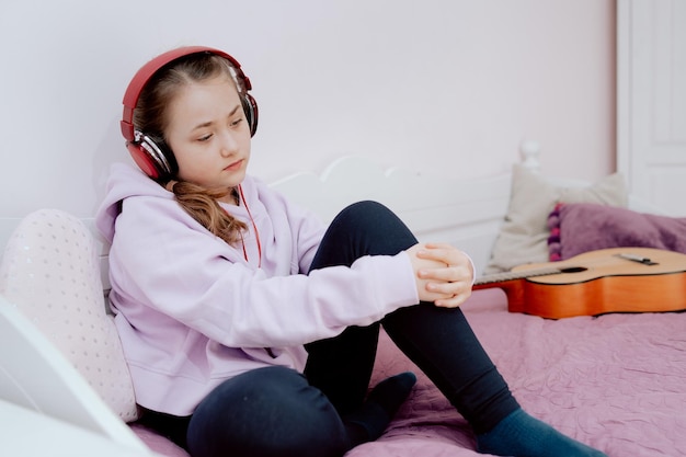 Smutna kaukaska nastolatka słucha muzyki siedząc na łóżku w swojej jasnej sypialni dziewczyny
