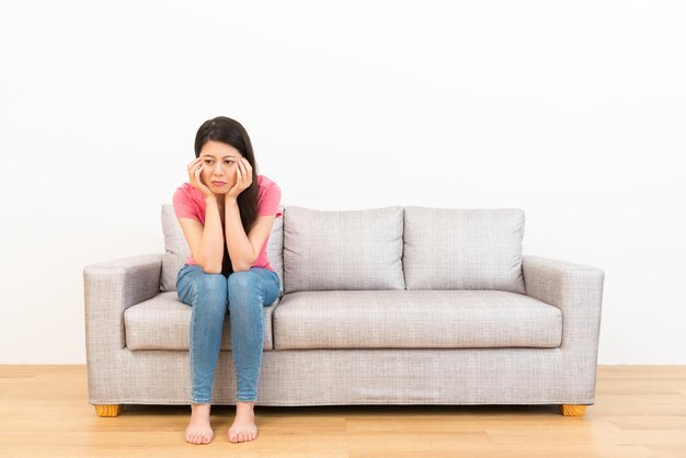 smutna kobieta siedzi na kanapie i płacze, myśląc o złych wieściach po tym, jak rodzina pokłóciła się w salonie podłoga z drewna z białym tłem.