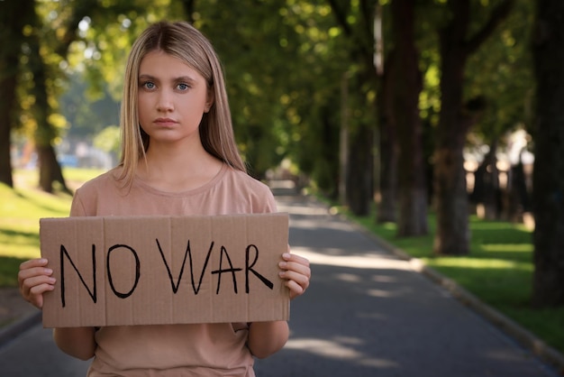 Zdjęcie smutna kobieta trzyma plakat ze słowami no war w parku miejsce na tekst