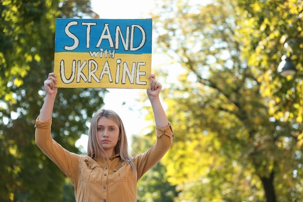 Zdjęcie smutna kobieta trzymająca plakat w kolorach flagi narodowej i słowa stań z ukrainą na zewnątrz przestrzeń dla tekstu