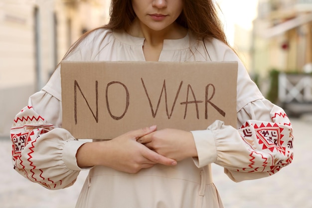 Zdjęcie smutna kobieta w haftowanej sukience trzymająca plakat no war na zbliżeniu ulicy miasta