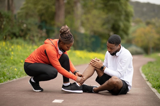 Smutna młoda Afroamerykanka robi masaż chłopakowi po urazie mięśni nóg w parku