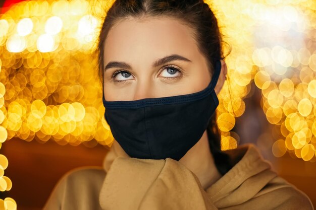 Smutna znudzona kobieta stoi na zewnątrz noc wieczorem zima w wakacyjnej atmosferze nosi niebieską maskę na twarz