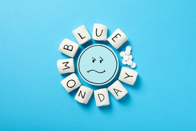 Smutne pigułki emoji i pianki z tekstem Blue Monday na niebieskim tle widok z góry