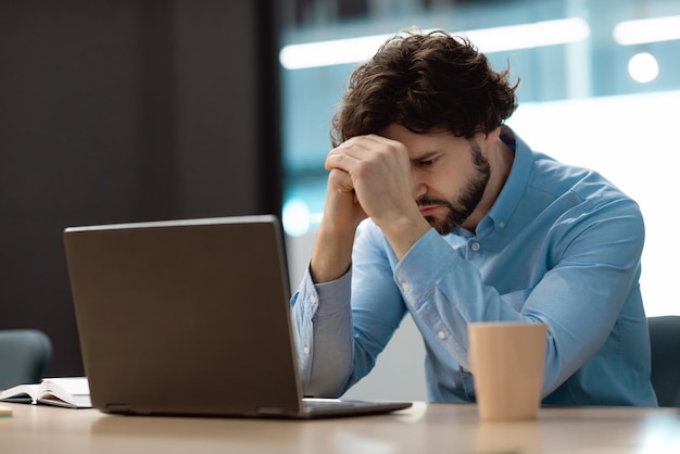 Smutny biznesmen chwytający głowę za pomocą laptopa