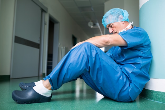 Smutny chirurg siedzi na podłodze w korytarzu