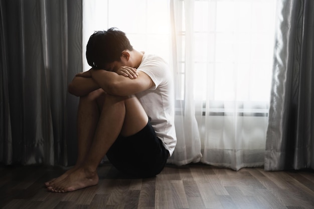Smutny i przygnębiony młody mężczyzna siedzący na podłodze w pokoju smutny nastrój czuję się zmęczony samotny i nieszczęśliwy koncept Selektywne skupienie