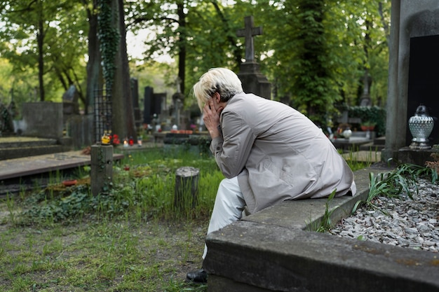 Zdjęcie smutny mężczyzna siedzący na grobie na cmentarzu