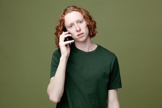 Smutny młody przystojny facet ubrany w zieloną koszulkę rozmawia przez telefon na białym tle na zielonym tle