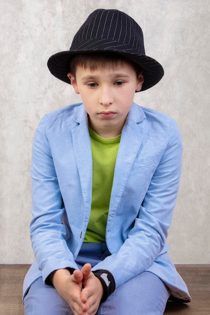 Smutny stylowy chłopak w eleganckim kapeluszu i niebieskim garniturze jest zamyślony