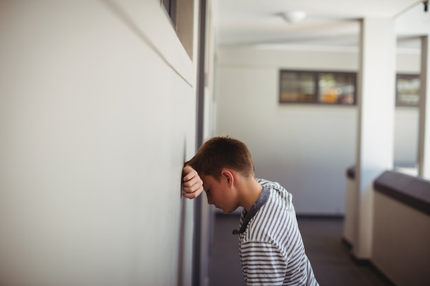 Smutny uczeń oparty głową o ścianę w korytarzu