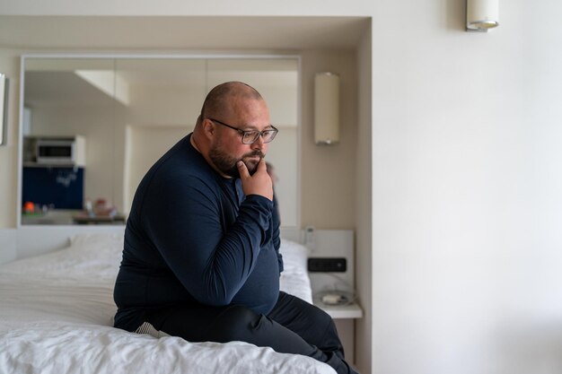 Smutny, zdezorientowany, przygnębiony mężczyzna siedzący w łóżku w domu i martwiący się o problemy życiowe.