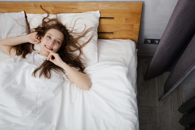 Śniąca dziewczyna leżąca na białym łóżku z dużymi poduszkami