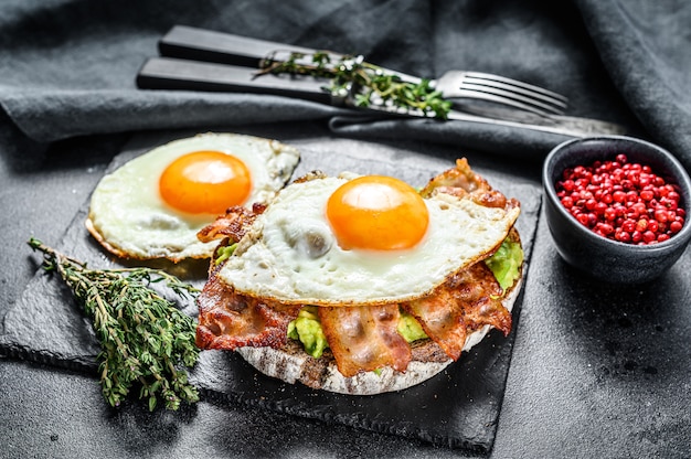 Zdjęcie Śniadanie angielskie, tost z bekonem, awokado i jajkiem na desce do krojenia.