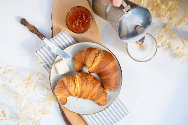Zdjęcie Śniadanie kontynentalne, filiżanka kawy z mlekiem, dwa rogaliki, masło i dżem pomarańczowy na desce, widok z góry