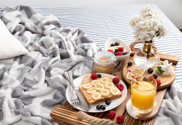 Śniadanie w łóżku. Drewniana taca ze szklanką soku pomarańczowego i kanapką z jagodami