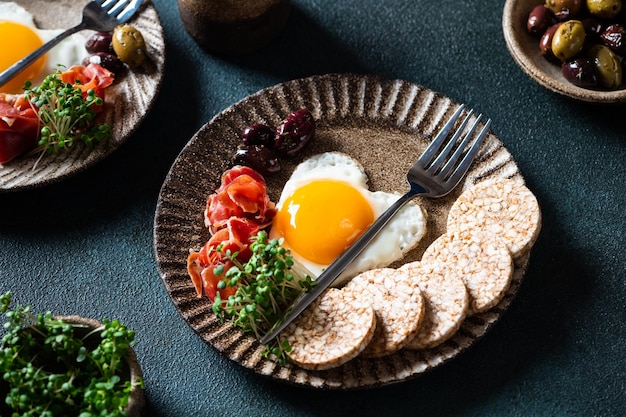 Śniadanie w Walentynki - jajka sadzone w kształcie serca i oliwki. Zdrowe śniadanie. Wafle ryżowe z jajkiem i hamonem. Romantyczne śniadanie. Widok z góry.