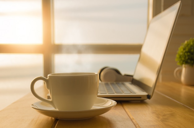Śniadanie z filiżanką ciepłej kawy na stole w biurze z laptopem.