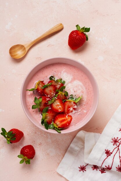 Zdjęcie Śniadanie z granolą, kokosem i truskawkowym smoothie w misce na różowej jasnej ścianie. wiosenne menu dietetyczne. widok z góry.