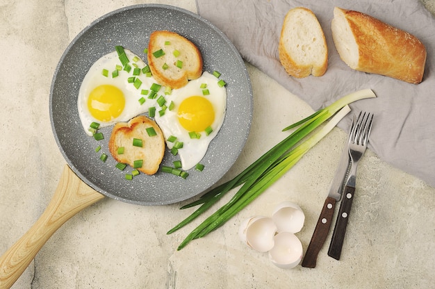Śniadanie z jajkiem sadzonym i zieloną cebulą oraz bagietką na szarej powierzchni