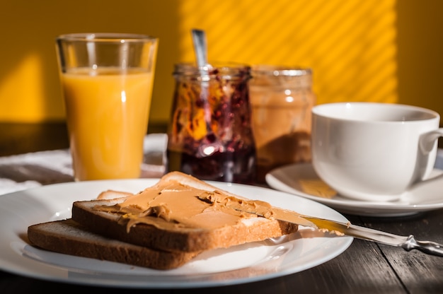 Śniadanie z masłem orzechowym i dżemem oraz filiżankę kawy na drewnianym stole w porannym słońcu