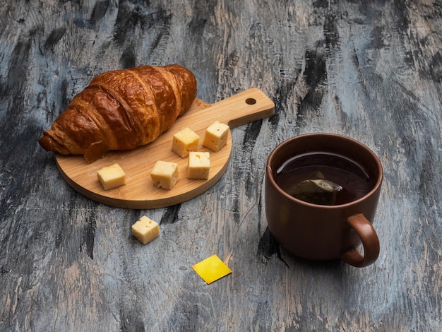 Śniadanie z plastrami sera croissant i herbatą w brązowym kubku