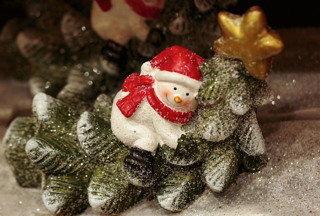 Śnieżak ozdobiony na Boże Narodzenie Mała figurka śnieżaka na niewyraźnym tle szczęśliwy śnieżak na wakacje zimowe choinka i światła w tle bokeh deszcz lekki śnieg i płatki śniegu