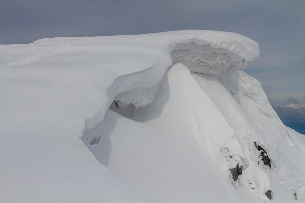 Śnieżny gzyms na pokrytym śniegiem zboczu góry w wysokich górach