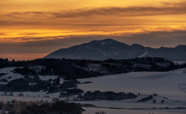 Śnieżny zimowy krajobraz górski i kolorowe niebo ze względu na wschód słońca nad wzgórzem Poludnica w Niskich Tatrach na Słowacji
