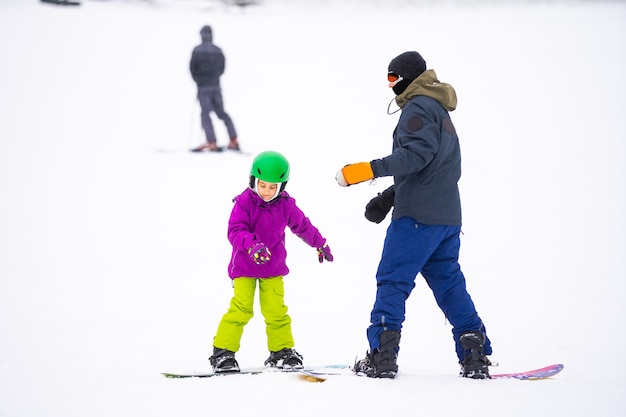 Snowboard Sporty zimowe. mała dziewczynka ucząca się snowboardu, nosząca ciepłe zimowe ubrania. Zimowe tło.