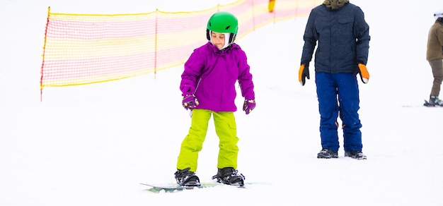 Snowboard Sporty zimowe. mała dziewczynka ucząca się snowboardu, nosząca ciepłe zimowe ubrania. Zimowe tło.