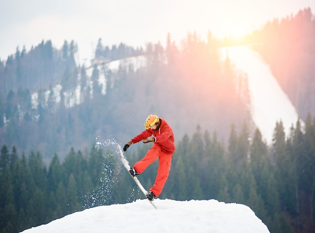 Snowboardzista człowiek skacze na szczycie śnieżnego wzgórza z snowboard wieczorem